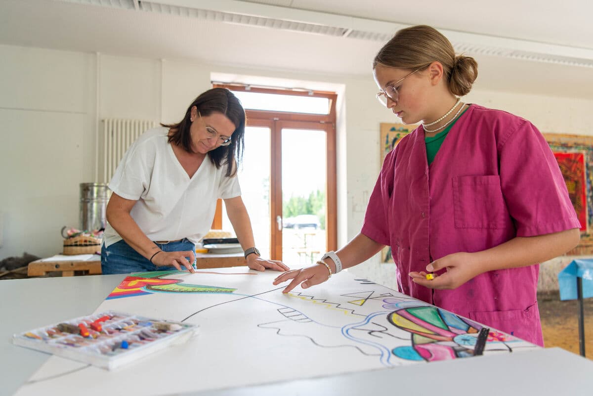 Eine Frau und ein Mädchen gestalten zusammen ein Bild während der Kunsttherapie.