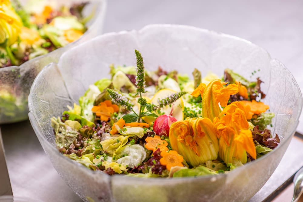 Frische bunte Salatschüssel mit verschiedenen Gemüsesorten und Blüten verziert