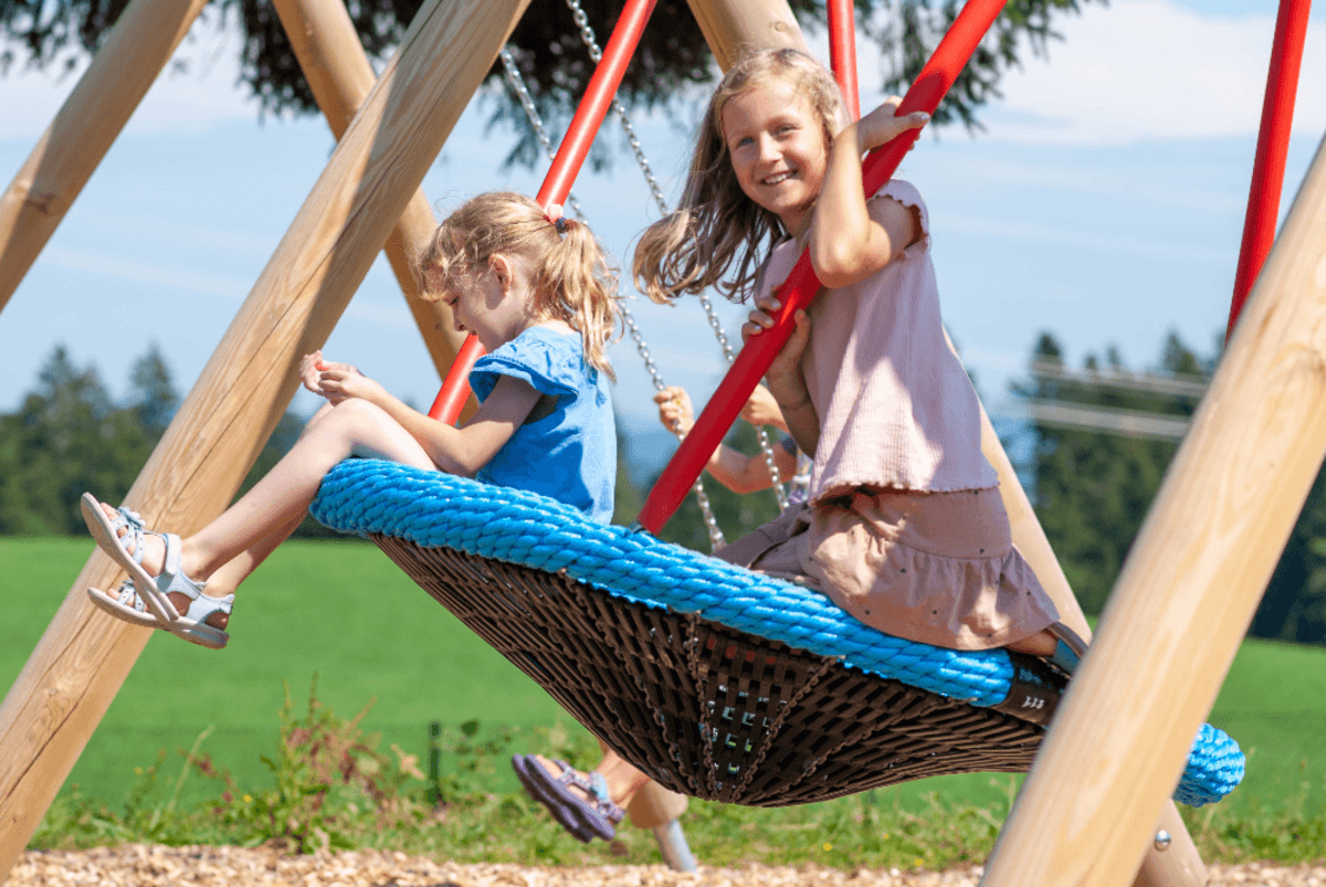 Zwei fröhlich-schaukelnde Kinder auf dem hauseigenem Spielplatz